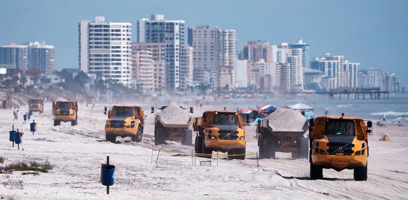 Large off road dump trucks run south empty as trucks roll north with a loads of sand on the Wilbur-by-the-Sea beach, Tuesday July 8, 2025 as the beach restoration porject moves along.