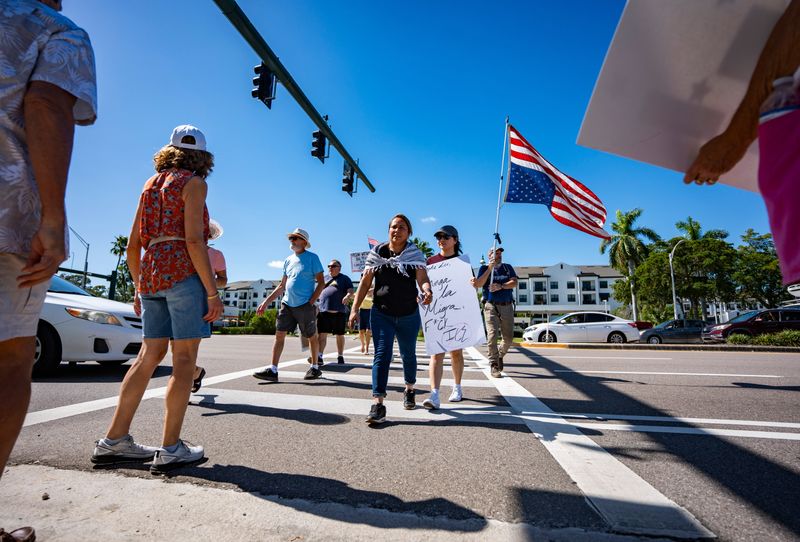 Protesters cross the street with their signage during the No Kings protest at the Collier County Government Center in Naples, Fla., on Saturday, Oct. 18, 2025.