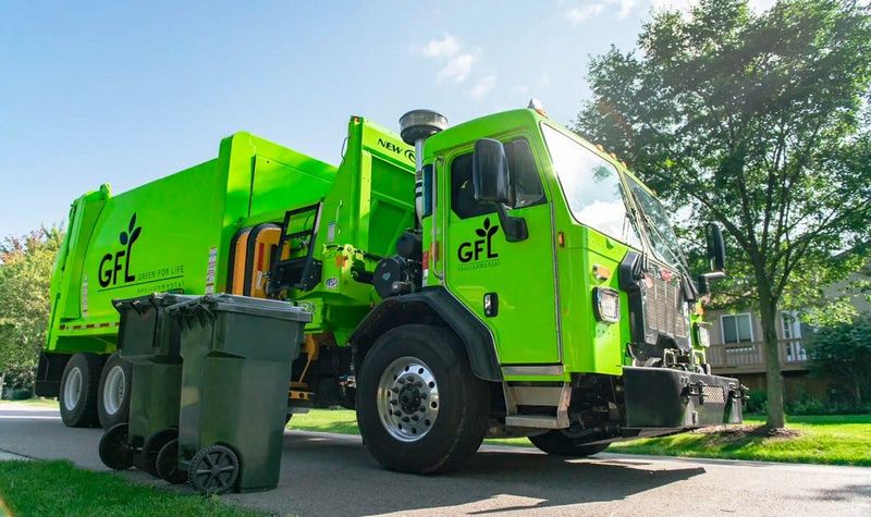 An Alachua County's waste hauler, GFL (Green For Life), is seen parked next to two trash bins.
