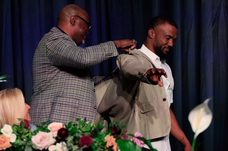 Former Florida running back Brandon James, right, is outfitted with his induction jacket from father Brian James as Jacksonville Mayor Donna Deegan looks on during the Florida-Georgia Hall of Fame induction ceremony, Friday, Oct. 31 2025, at the Hyatt Regency Jacksonville Riverfront in Jacksonville, Fla.