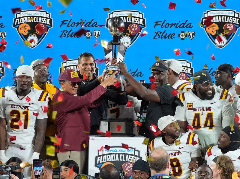 Bethune-Cookman President Dr. Albert Mosley (from left), athletic director Reggie Theus and head coach Raymond Woodie Jr. raise the trophy after winning the game against Florida A&M during the Florida Classic, Saturday, Nov. 22, 2025, at Camping World Stadium in Orlando.