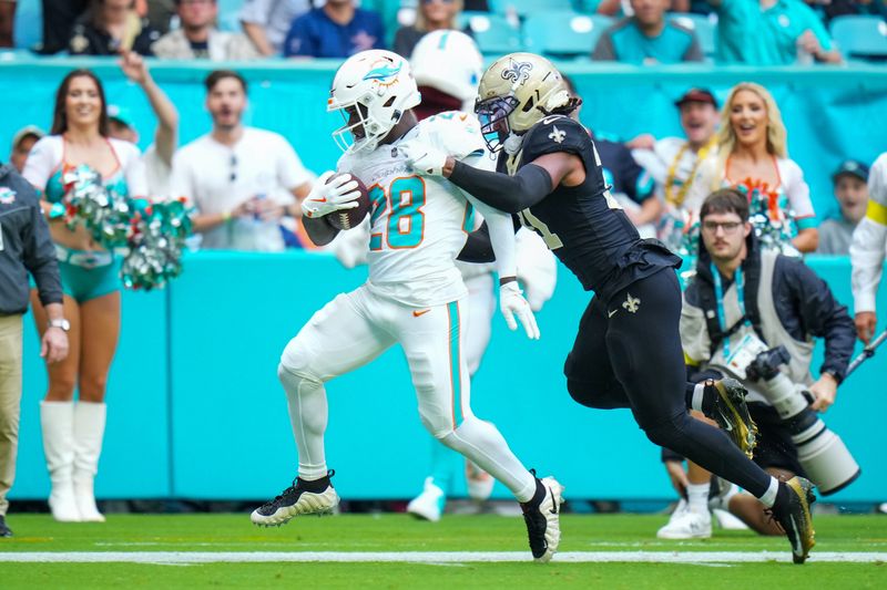 Nov 30, 2025; Miami Gardens, Florida, USA; Miami Dolphins running back De'Von Achane (28) scores a touchdown as New Orleans Saints safety Jordan Howden (31) defends during the first half at Hard Rock Stadium. Mandatory Credit: Rich Storry-Imagn Images