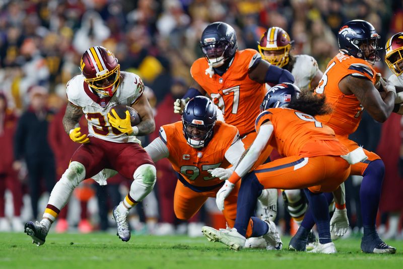 Nov 30, 2025; Landover, Maryland, USA; Washington Commanders running back Chris Rodriguez Jr. (36) carries the ball defended by Denver Broncos defensive tackle D.J. Jones (93) and safety Talanoa Hufanga (9) in the second quarter of the game at Northwest Stadium. Mandatory Credit: Peter Casey-Imagn Images