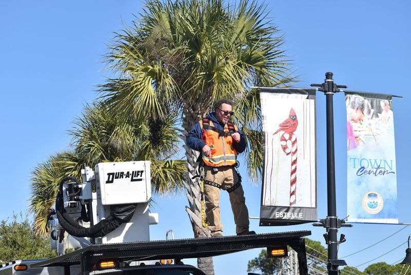 Brandon Moore of the city of Destin hangs up one of many holiday-themed banners along Main Street on Dec. 9.