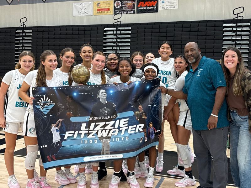 The Jensen Beach High girls basketball team joins Lizzie Fitzwater (bottom row, second from the left) for a photo after she eclipsed 1,000 career points during the Falcons' 52-30 win over Fort Pierce Central on Friday, Dec. 12, 2025 from Jensen Beach High School.