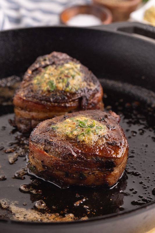 Tender filet mignon is wrapped in smoky bacon, seared in a cast-iron skillet, and finished with a rich cowboy butter.