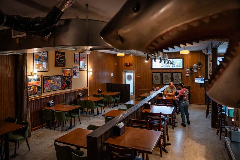 Indoor dining area at the new location of Tropical Smokehouse in Delray Beach, Fla., on January 15, 2025. A large shark adorns a wall near the condiments.