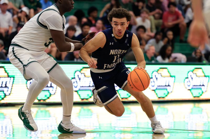 North Florida Ospreys guard Kamrin Oriol (11) dribbles against Jacksonville Dolphins forward Donovan Rivers (33) during the second half of an NCAA men’s basketball game at Swisher Gymnasium, Saturday, Feb. 14, 2026, in Jacksonville, Fla. JU held off UNF 63-56. [Corey Perrine/Florida Times-Union]