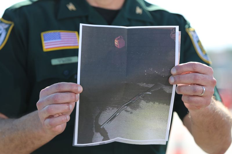 A Palm Beach County Sheriff’s deputy holds a photo of a shotgun and gas can they say an intruder brought onto Trump’s Mar-a-Lago estate.