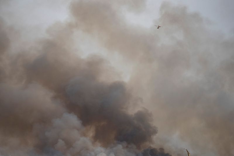 A helicopter flies overhead as smoke billows from a 24,000-acre brushfire in Big Cypress National Preserve on Wednesday, Feb. 25, 2026.
