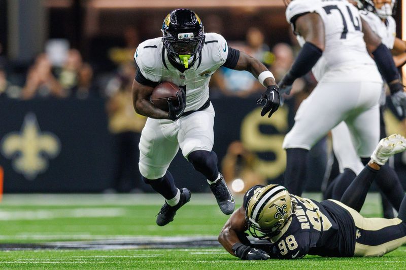Aug 17, 2025; New Orleans, Louisiana, USA; Jacksonville Jaguars running back Travis Etienne Jr. (1) leaps to avoid the tackle of New Orleans Saints defensive end Chris Rumph II (98) during the first half at Caesars Superdome. Mandatory Credit: Stephen Lew-Imagn Images