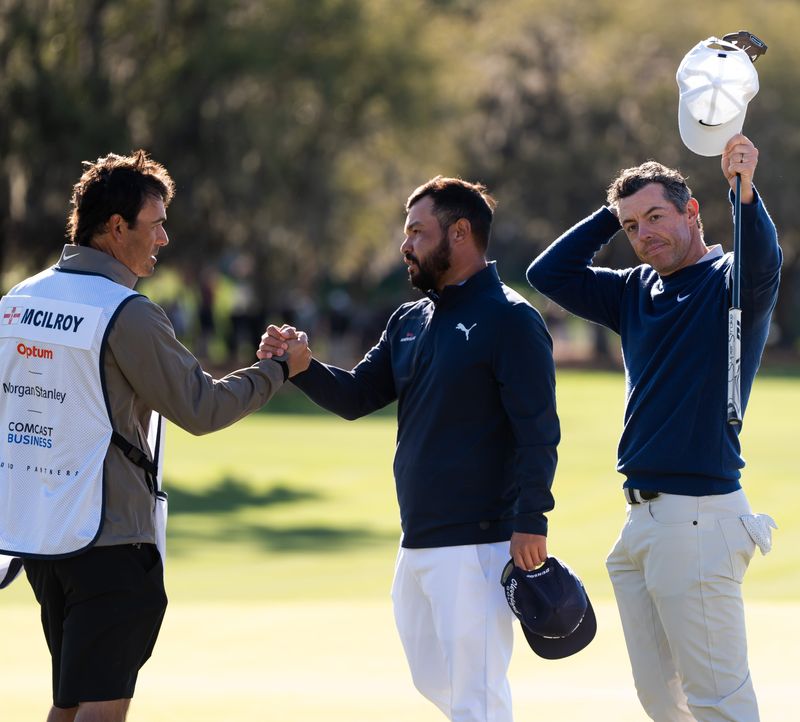 Rory McIlroy raises his putter and hat after defeating J.J. Spaun in a three-hole aggregate playoff of the Players Championship at TPC Sawgrass Monday March 17, 2025 in Ponte Vedra Beach, Fl. McIlroy's caddie Harry Diamond shakes hands with Spaun.