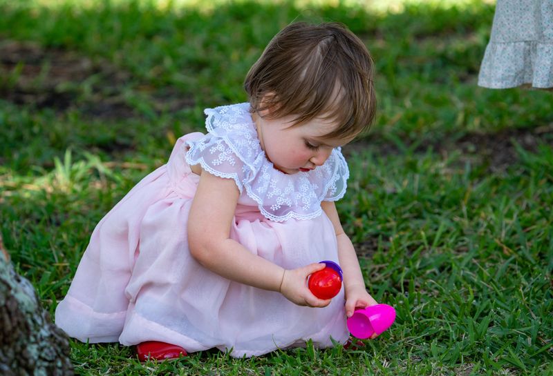 A girl kneels to open treats in the lawn during the annual Easter Egg Hunt at the Flagler Museum Saturday April 4, 2026.