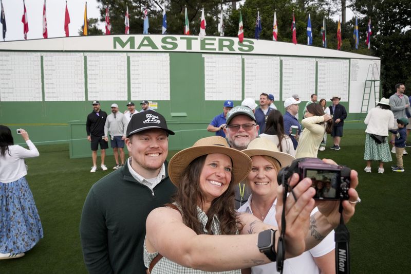 Apr 7, 2026; Augusta, Georgia, USA; Seth Cory (from left) and his wife, Corrin, Renee Cory and her husband Darrell take a photograph in front of the Masters scoreboard during a practice round for the Masters Tournament at Augusta National Golf Club. Mandatory Credit: Grace Smith-Imagn Images