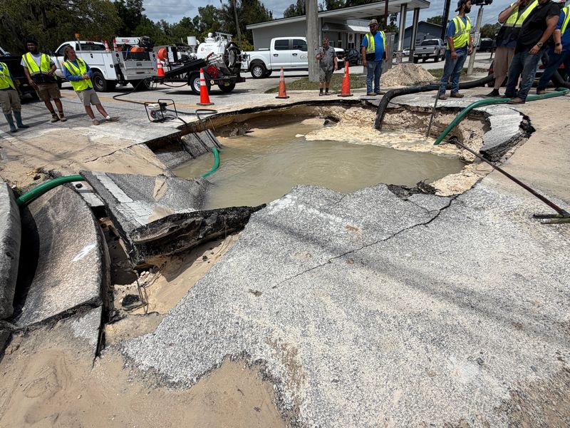 Officials stand near a hole in the ground around State Road 15A and Euclid Avenue in DeLand.