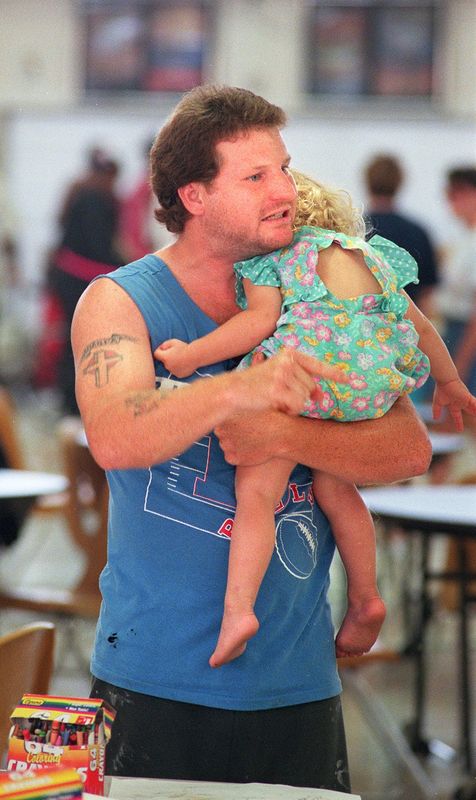 On July 5, 1998, Todd Findley, an evacuee from Daytona North in Flagler County, holds one of his three children, 2-year-old Brittany, in the Palatka High School Red Cross evacuation center. He was frustrated because instead of seeing information on the television about the wildfires and his community, the only news available was a video clip of President Bill Clinton talking about China and democracy.