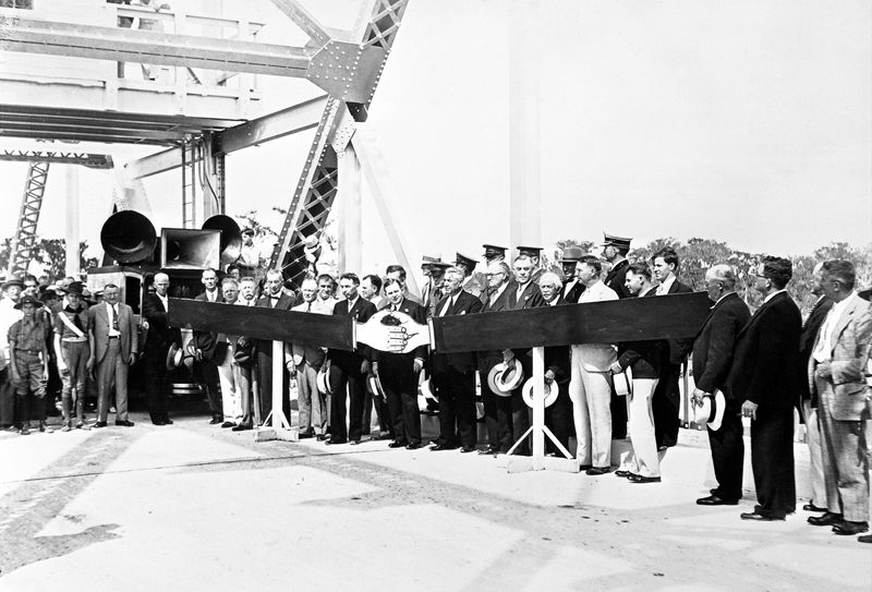 Hands across the water. Seminole County Commission Chairman John Meisch, and Volusia County Commission Chairman Ben Thursby greet each other at the ceremonial opening of the Lake Monroe Bridge, April 6, 1934, as Gov. David Sholtz (center, by the cartoon hands) and state Cabinet members look on.