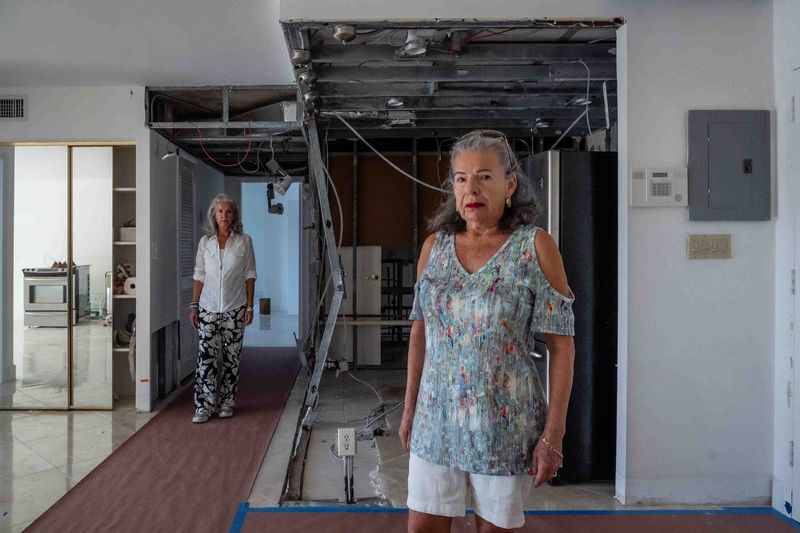 Amelia Owens, right, stands in front of what was her kitchen in condo 2V at Boca View Condominium in Boca Raton, Fla., on May 6, 2025. She's been unable to sell the unit she once shared with her late husband because the HOA president has repeatedly blocked sales. Owens sister Laura Rodriguez, left, stands in the condo.