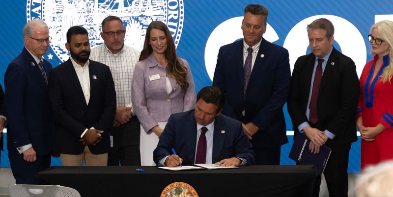 Florida Gov. Ron DeSantis signs SB 484, a measure that sets guidelines for large data centers, during an event May 7 at Florida Polytechnic University in Lakeland. Florida Poly President Devin Stephenson, left, joins other local officials in watching the signing.