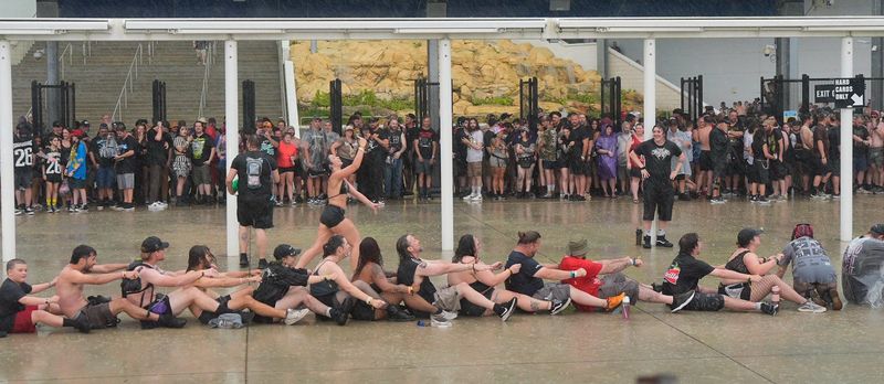 As the rain comes down, Welcome to Rockville fans mimic rowing a boat at Daytona International Speedway in Daytona Beach on Friday, May 8, 2026. Heavy storms moved into the area, halting evening performances.