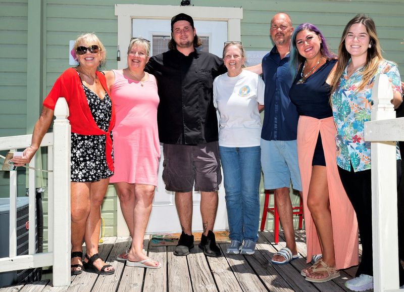Five beloved downtown Sarasota bungalow businesses are planning a major move following the announcement of a new apartment complex that would displace them. From left: Wendy Lee Goldberg, Tammy Hauser, René Zimmermann, Cathy Vande Mheen, Tim and Tess Craig, and Jazz Wingard pose on the front porch of Discover Sarasota Tours.