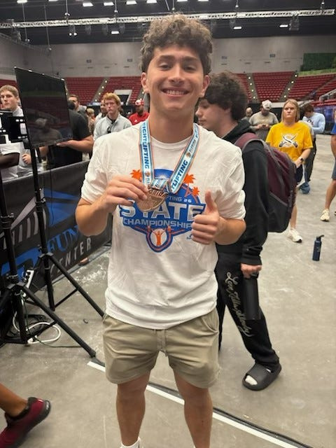 Ridgeview's Micah Davis, wearing blue and the medal, placed third in Class 1A state weightlifting in the Olmpyic category on Friday, May 8, 2026, at the RP Funding Center.