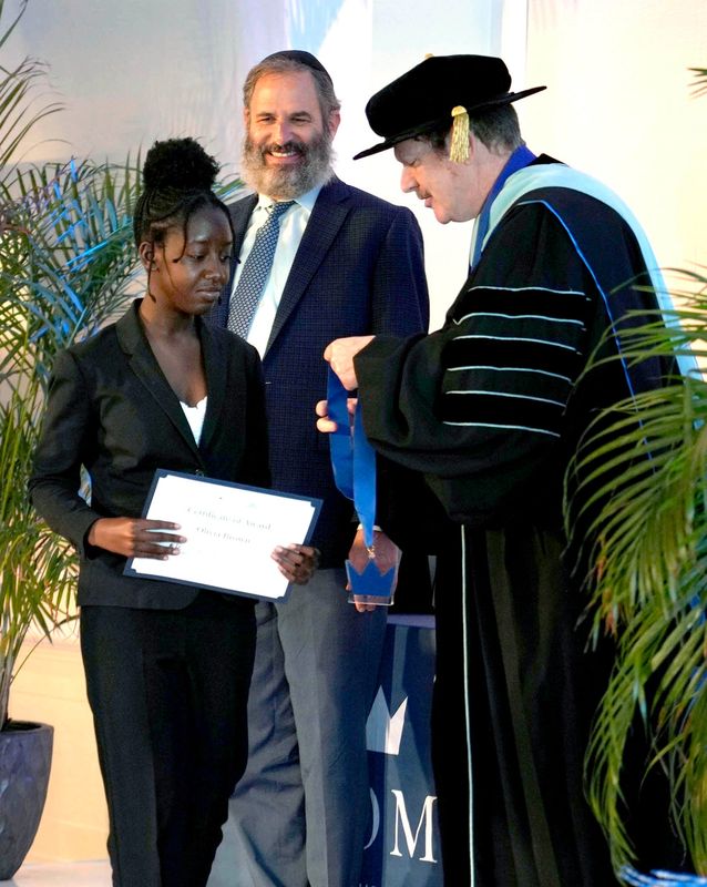 Olivia Brown, left, collects her certificate and medal from Rabbi Moshe Scheiner and Art Johnson during the Solomon Leadership program graduation ceremony at Palm Beach Synagogue on April 28 in Palm Beach.