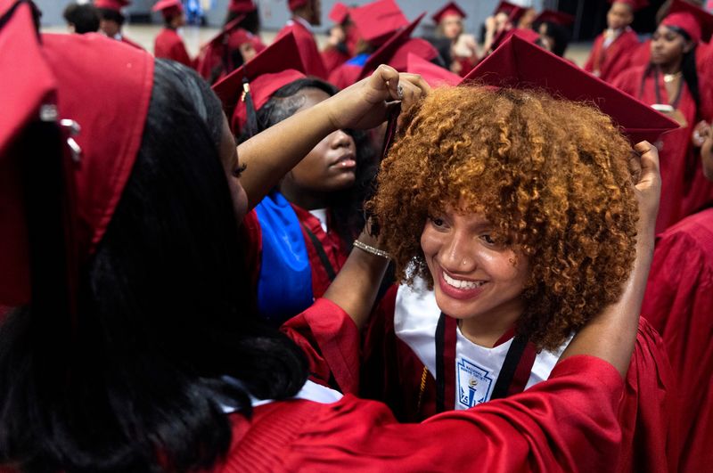 Yvellah Semeah, right, get help with her cap from Rachelle Cheriza and Amanda Volmar before the Palm Beach Central High School graduation ceremony at the South Florida Fairgrounds on May 15, 2026, in suburban West Palm Beach, Florida.
