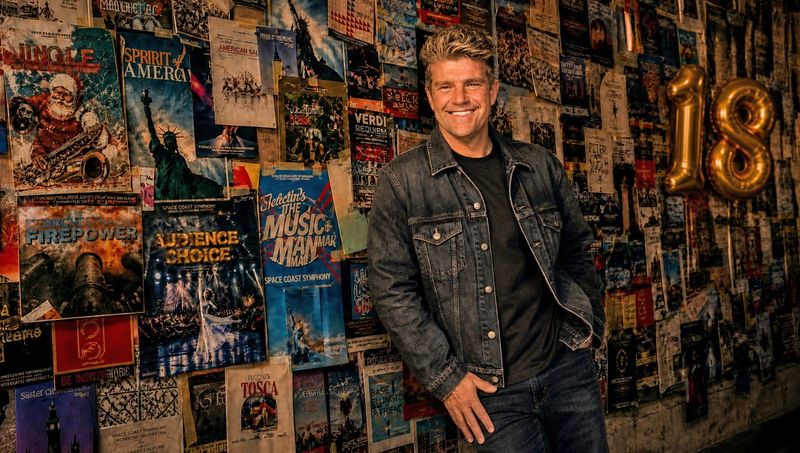 Conductor Aaron Collins of the Space Coast Symphony Orchestra is surrounded by program covers and graphics from past seasons. The orchestra has announced the programming for its 18th season, with performances in both Indian River and Brevard Counties.