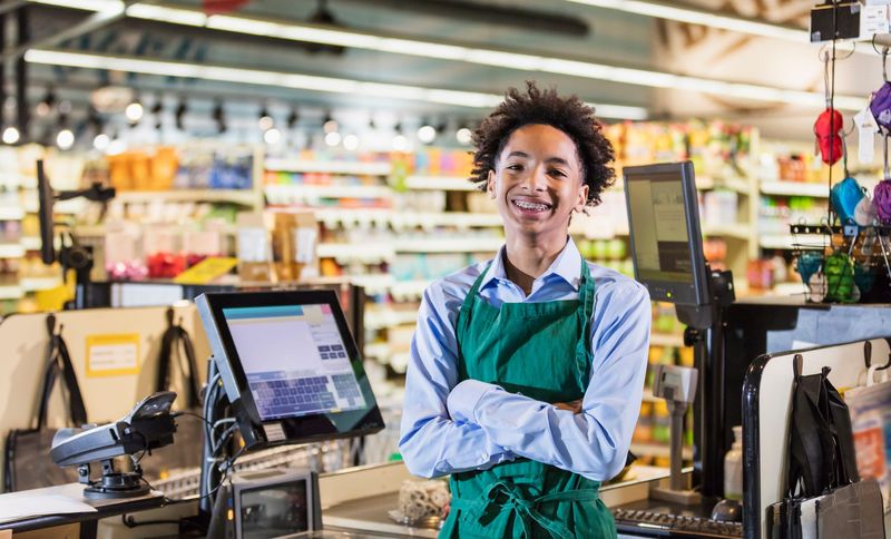 A teenage boy works in a supermarket at the checkout counter.