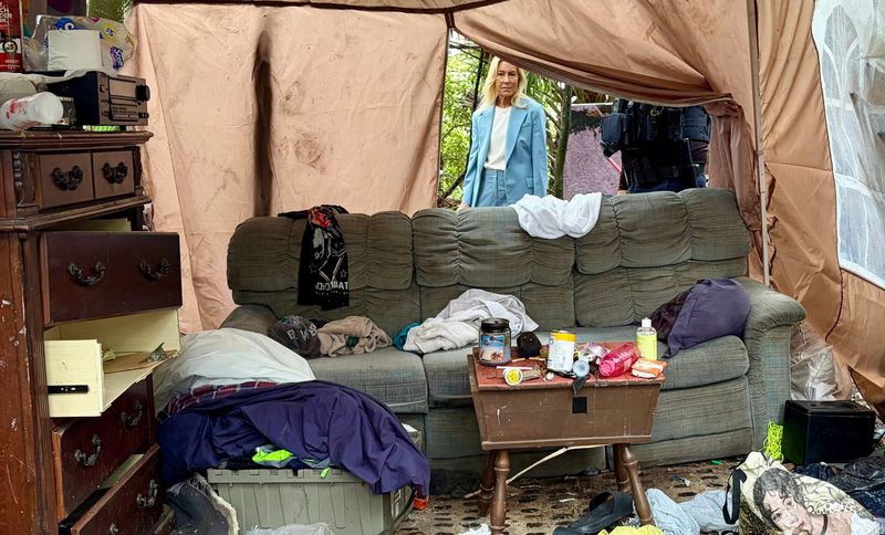 Jacksonville Mayor Donna Deegan looks through an opening in a tent at a homeless camp shelter in woods off North Main Street on June 1, 2026. The city will use newly purchased equipment to help clear piles of debris spread around the tent in an area near homes on the side of a fence.