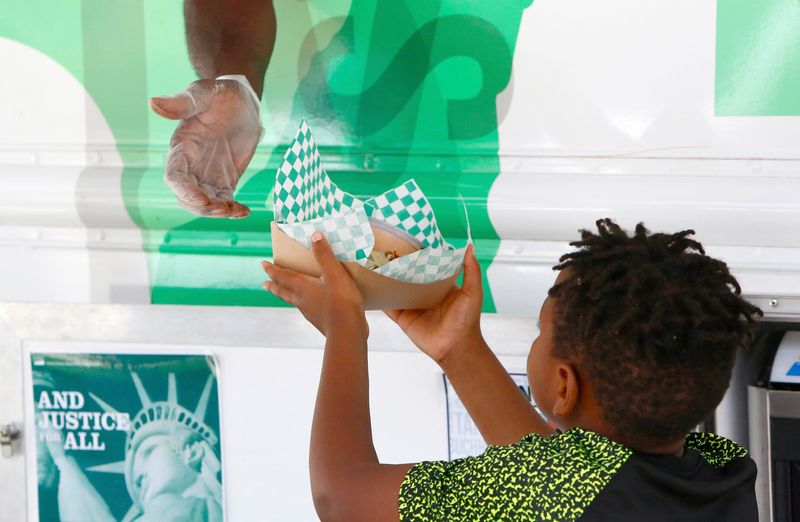 A food service assistant hands a free lunch to a kid from the On The Point food truck outside the SWAG Center in the Linton Oaks neighborhood of Gainesville Fla., June 18, 2019. The Alachua County Public Schools Food and Nutrition Services, which has for years provided free meals to kids through the Summer Meals program, is now continuing the second year of the food truck program that brings free meals to neighborhoods that can't easily get to some of the schools where meals are provided.
