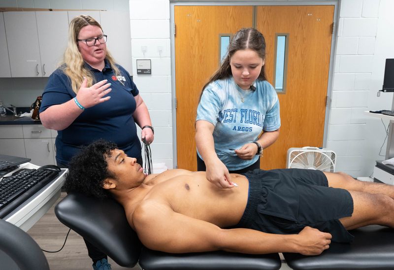 Who We Play For heart screening director Jessica Landingham, left, instructs Caitlin Creaser as she places electrodes on fellow UWF student Isaiah Jones as they demonstrate how an electrocardiogram (ECG) is performed at the University of West Florida in Pensacola on June 3, 2026.