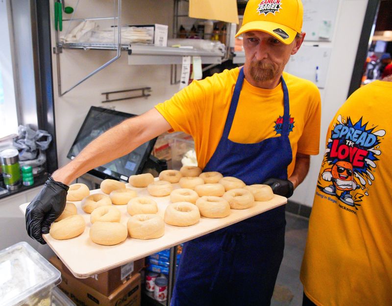Micah Shepherd carries a sheet of freshly made bagels to the boiler at Bang'N Bagel Co., located at 13423 Beach Boulevard, Unit 204 in Jacksonville, Fla. Thursday, June 4, 2026. [Doug Engle/Florida Times-Union]