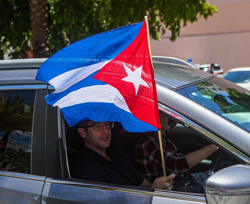 An automobile passenger waves a Cuban flag at people at West Palm Beach city hall taking part in rally to support anti-government protesters in Cuba, Sunday, July 18, 2021.