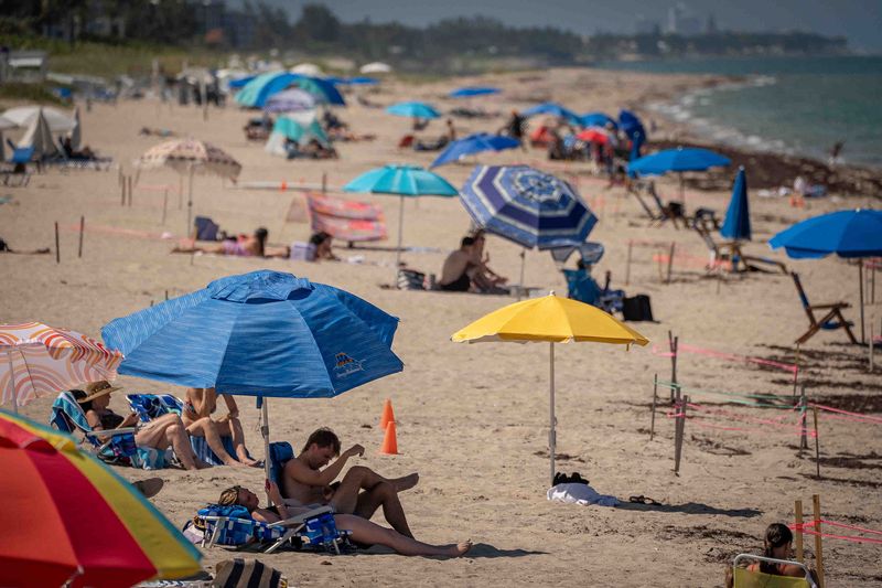 Beachgoers sit in the sunshine and under umbrellas in Lake Worth Beach, Fla., on June 22, 2026. Temperatures are reaching record highs across Palm Beach County to start the week.