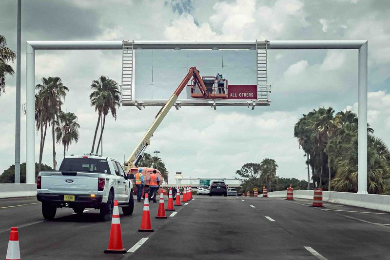Workers remove the last of the red sign on the board on the entrance roads to Palm Beach International Airport in unincorporated Palm Beach County, Fla., on June 24, 2026.
