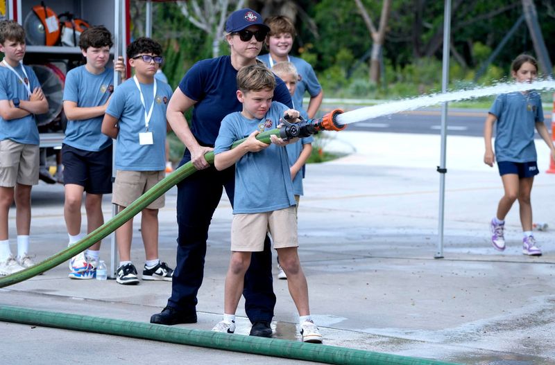 Demitrious Gonzalez, helps a participant use a charged firehose during The Police and Fire Youth Academy at the South Fire Station on June 16 in Palm Beach. The two-day program is for children ages 8 through 12 who attend school on the island.