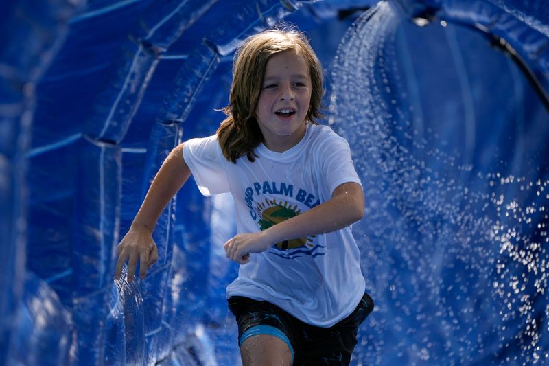 Oakley Hill, 8, cools off in a waterslide during Camp Palm Beach.