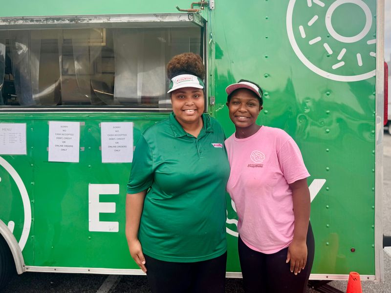 Krispy Kreme Assistant Manager Jamayiah Cooley (left) and Supervisor Alyssia Cooley pose for a photo in front of Krispy Kreme's doughnut trailer, parked next to its iconic Daytona Beach store.