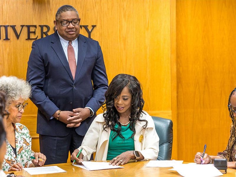 FAMU President Marva Johnson sits with Dr. Celeste Hart, daughter and granddaughter of the two noted doctors whose medical practice was housed in the Brickler building, as she signs the documents giving FAMU ownership of the historic site. Kelvin Lawson, FAMU's  executive vice president and chief operations officer, stands behind Johnson.