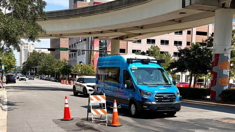 A NAVI transit shuttle moves to a different lane to avoid a pothole barricade while traveling down Bay Street in downtown Jacksonville on July 31, 2026. The Jacksonville Transportation Authority completed the first year of NAVI service and is studying whether to expand it to the elevated Skyway whose elevated structure is shown where it crosses Bay Street.