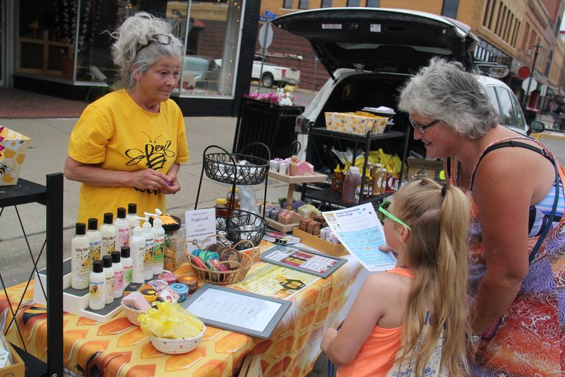 Families ask questions at the Spring Valley Honey booth as part of Iowa PBS' bingo game during the Perry Farmers Market on Thursday, June 13, 2024.