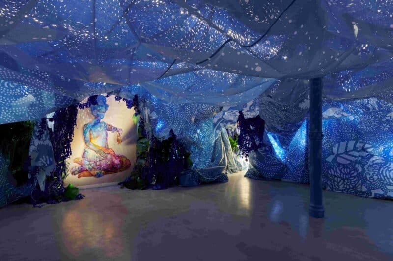 A Drexcyen chronocommons (To win the war you fought it sideways), 2019, by Firelei Báez features two paintings, hand-painted wooden frame, perforated tarp, printed mesh, handmade paper over found objects, plants, and books.