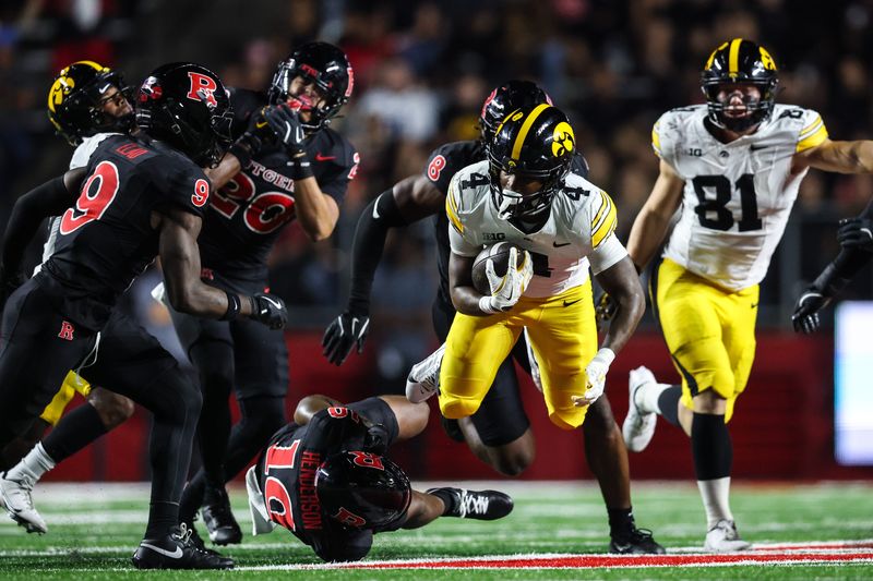 Sep 19, 2025; Piscataway, New Jersey, USA; Iowa Hawkeyes running back Jaziun Patterson (4) fights for yards as Rutgers Scarlet Knights defensive back Davoun Fuse (19) and defensive back Jett Elad (9) pursue during the first half at SHI Stadium. Mandatory Credit: Vincent Carchietta-Imagn Images