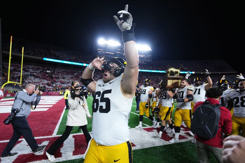 Oct 11, 2025; Madison, Wisconsin, USA; Iowa Hawkeyes offensive lineman Logan Jones (65) celebrates a win after the game against the Wisconsin Badgers while teammates carry The Heartland Trophy in the background at Camp Randall Stadium. Mandatory Credit: Ross Harried-Imagn Images