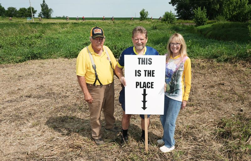 Scott Porter, a RAGBRAI rider who as a Grinnell College student calculated the exact center of Iowa, with landowners Loren and Ruth Book at the exact point near as RAGBRAI passes by on Day 4 on July 22, 2026.