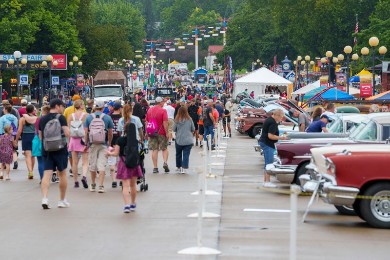 Fairgoers walk past cars on display during a break in the rain on Day 2 of the Iowa State Fair Friday, Aug. 14, 2026.