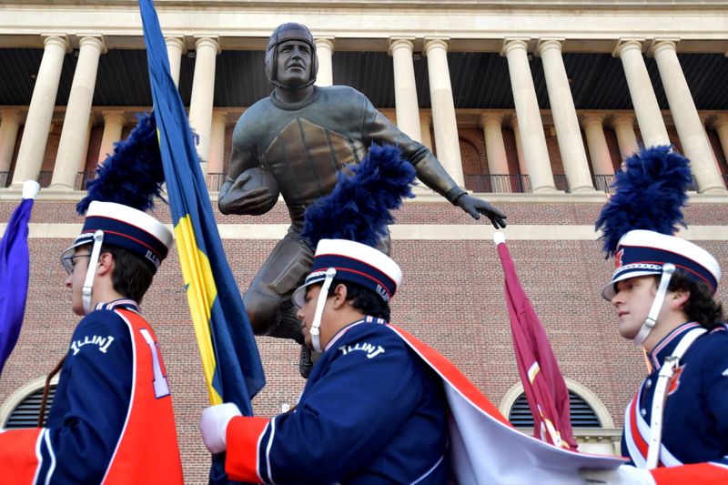 Nov 2, 2024; Champaign, Illinois, USA; Members of the Marching Illini Band walks past the statue of Red Grange outside the stadium before the start of a game with the Minnesota Golden Gophers at Memorial Stadium. Mandatory Credit: Ron Johnson-Imagn Images
