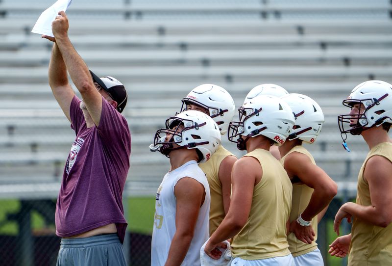 Dunlap players look over a play sheet held up by a coach on the official opening day of high school football practice Monday, Aug. 11, 2025 at Dunlap High School.